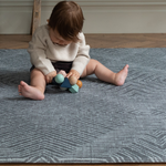 Baby sits up on Eclipse play mat for hard wood flooring and enjoys exploring wooden beaded baby toy