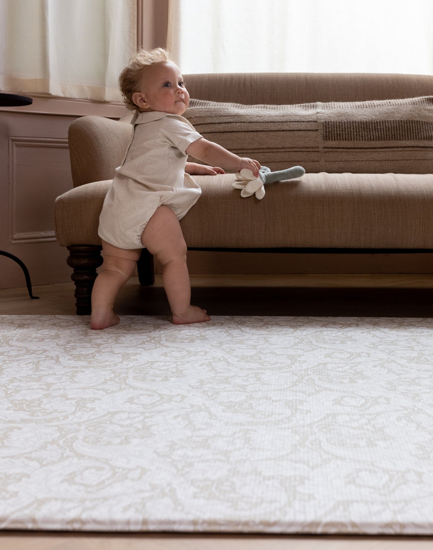 baby pulling up on sofa to standing on large padded play mat