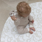 baby sitting on round neutral foam play mat with William Morris Bachelors Button design