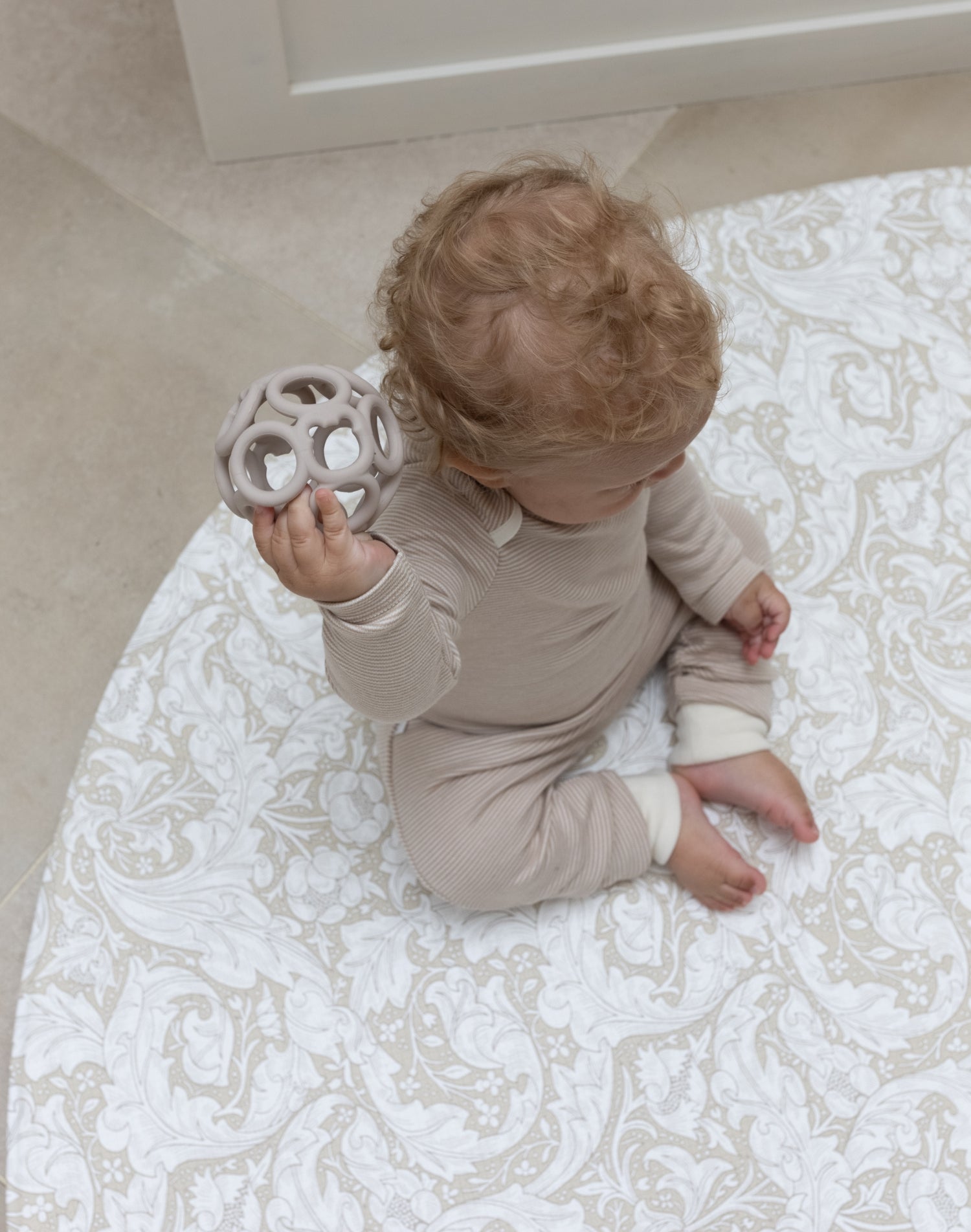 baby sitting on round neutral foam play mat with William Morris Bachelors Button design