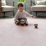 Baby sits on padded play mat enjoying playtime with metallic sensory toys