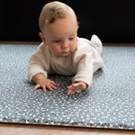 Baby lays on tummy on supportive play rug with leopard print design