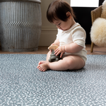 Baby plays with wooden toy while keeping cushy on play mat for kids by totter and tumble with green leopard design