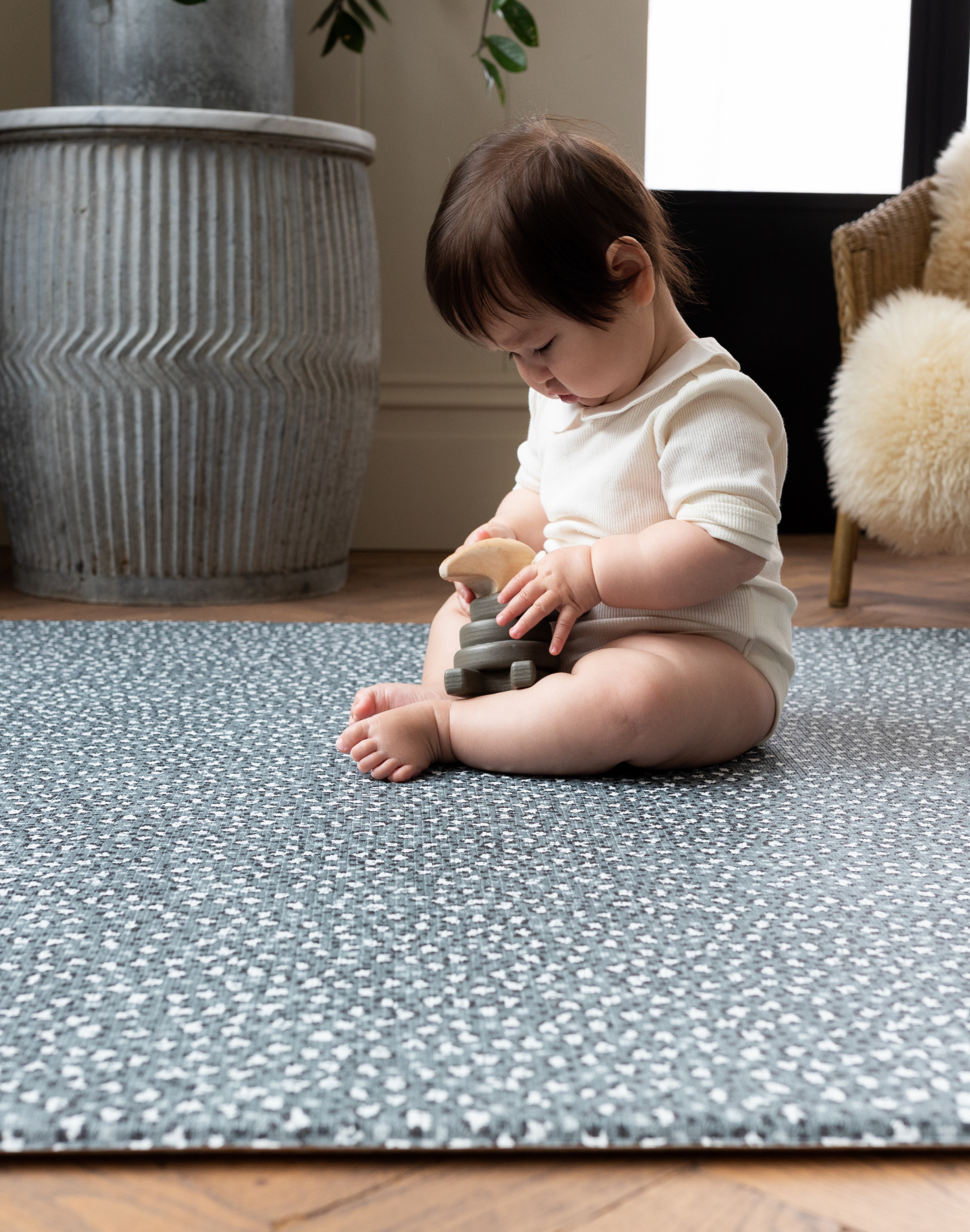 Baby plays with wooden toy while keeping cushy on play mat for kids by totter and tumble with green leopard design