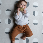 Little baby relaxes on a thick padded play mat while chewing on non toxic teething toy