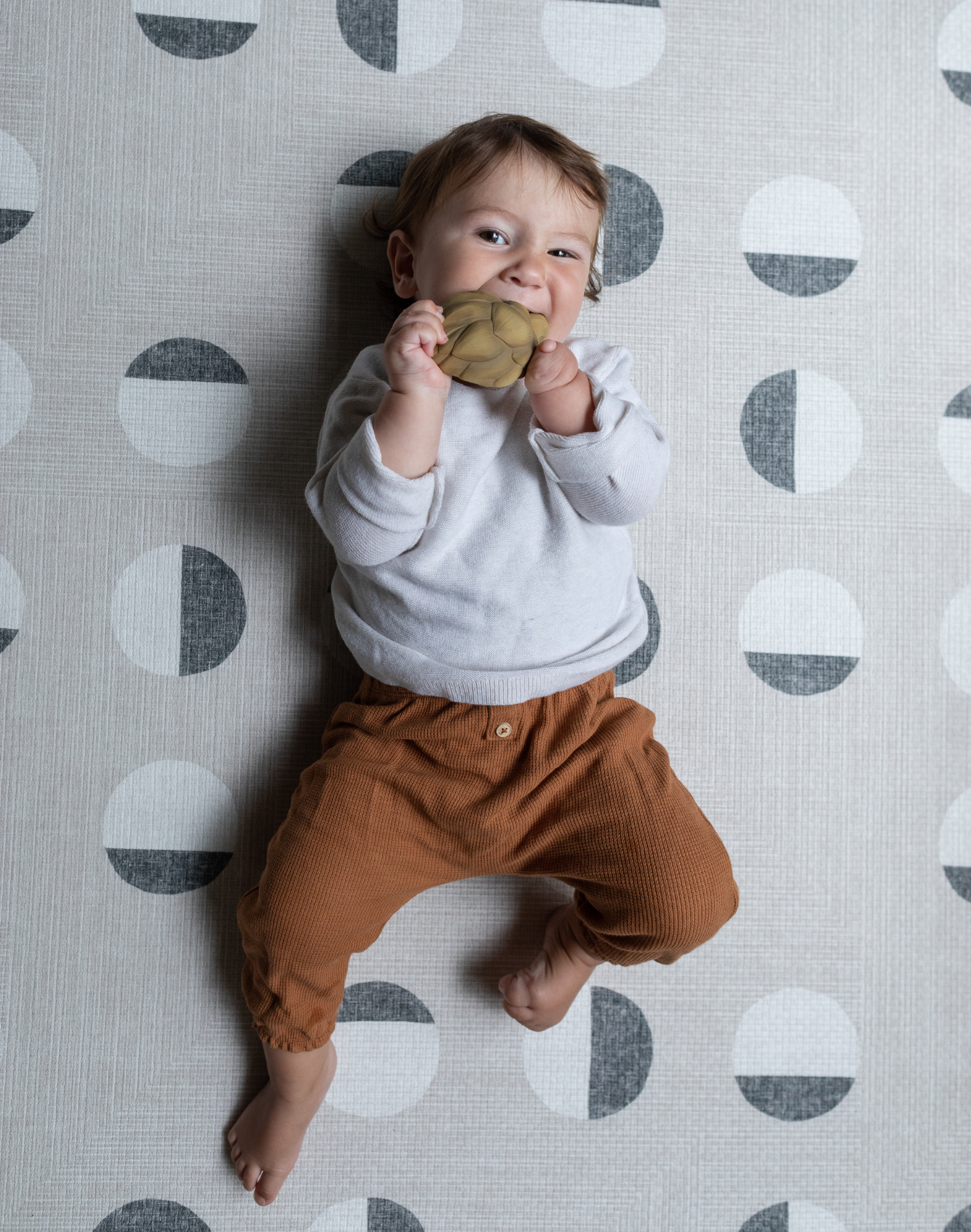 Little baby relaxes on a thick padded play mat while chewing on non toxic teething toy