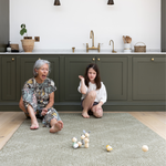 Little girl and grandmother enjoy playing with wooden skittles on a thick kitchen mat large in size for play time