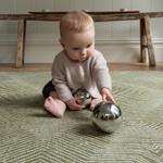 Baby enjoys playing with shiny sensory toys and is supported by the green floor rug by Totter and Tumble