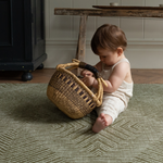 Baby enjoy play time with a basket on the cushy baby play mat with a contemporary green kilim design