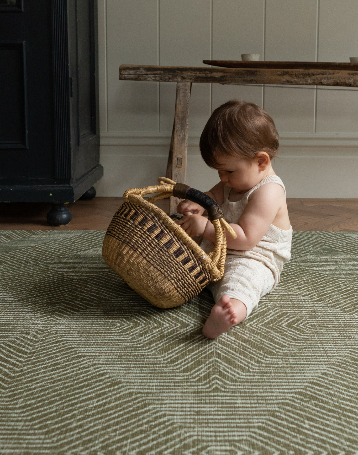 Baby enjoy play time with a basket on the cushy baby play mat with a contemporary green kilim design