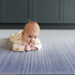 Baby enjoying tummy time on The Kasuri a large padded floor mat by Totter and Tumble adds a stylish appeal to the space it is unrolled in with a one piece design that is washable so spillages are easy to clean the perfect play rug for the home