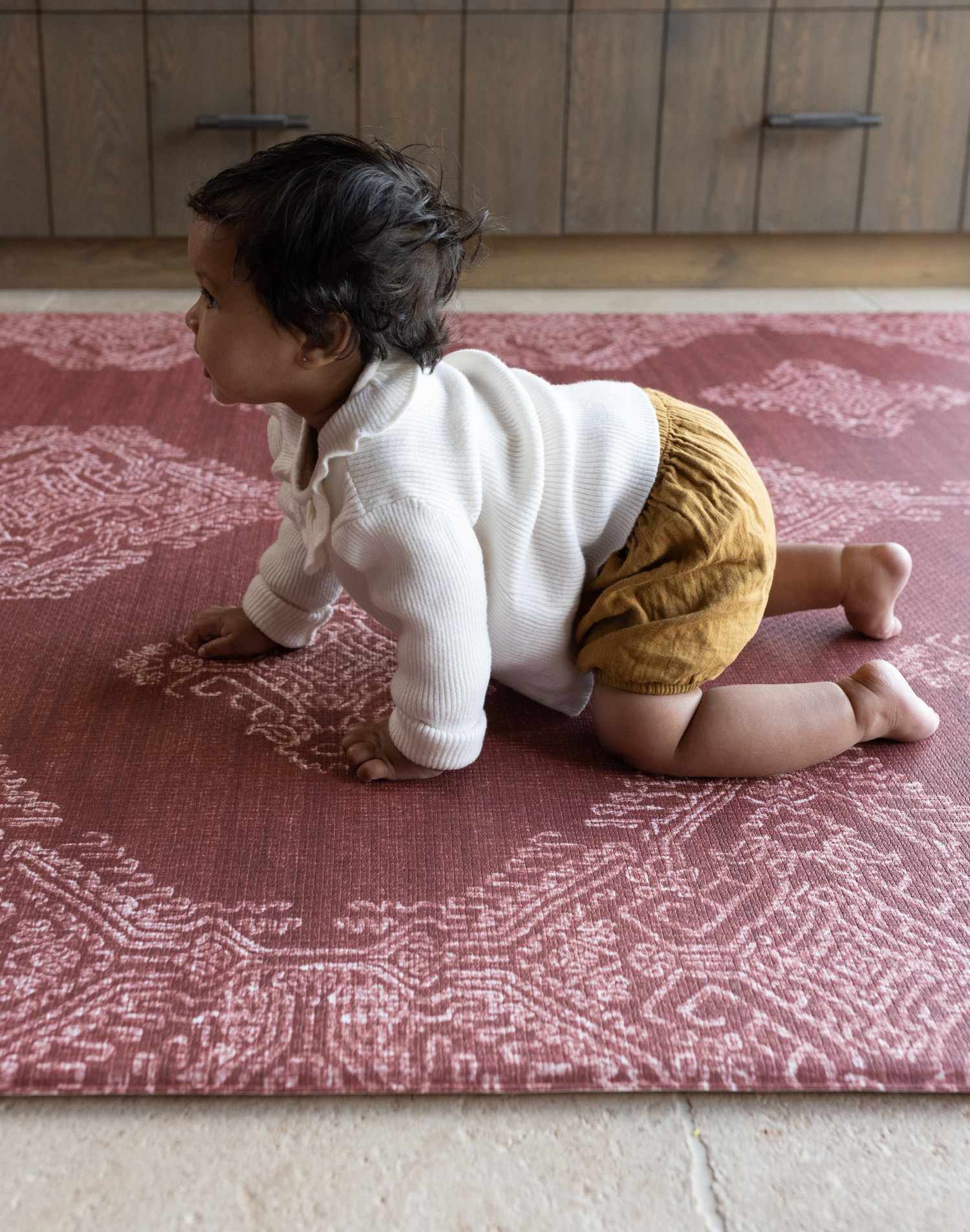 Large crawling play mat in a deep red tone with baby girl crawling across the protective and padded foam surface for safe and comfortable play time on any type of flooring