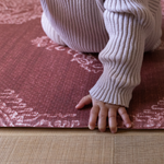 Baby holds onto edge of thick memory foam play mat that provides protection for floor time as little ones begin to move and explore 