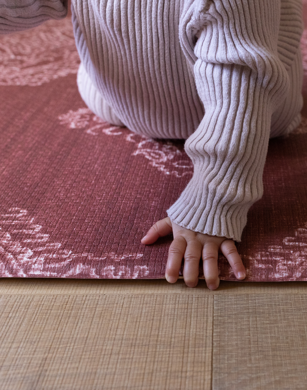 Baby holds onto edge of thick memory foam play mat that provides protection for floor time as little ones begin to move and explore 