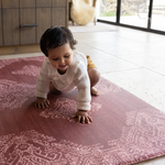 Baby crawls across textural play mat that looks like a rug in the kitchen with thick foam for support while exploring the floor beautiful red play mat design complements the boho style kitchen