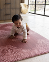 Baby crawls across textural play mat that looks like a rug in the kitchen with thick foam for support while exploring the floor beautiful red play mat design complements the boho style kitchen