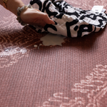 hand wipes up milk spill on surface of red play mat with intricate batik motif to creating a playmat that looks like a rug but practical for family homes