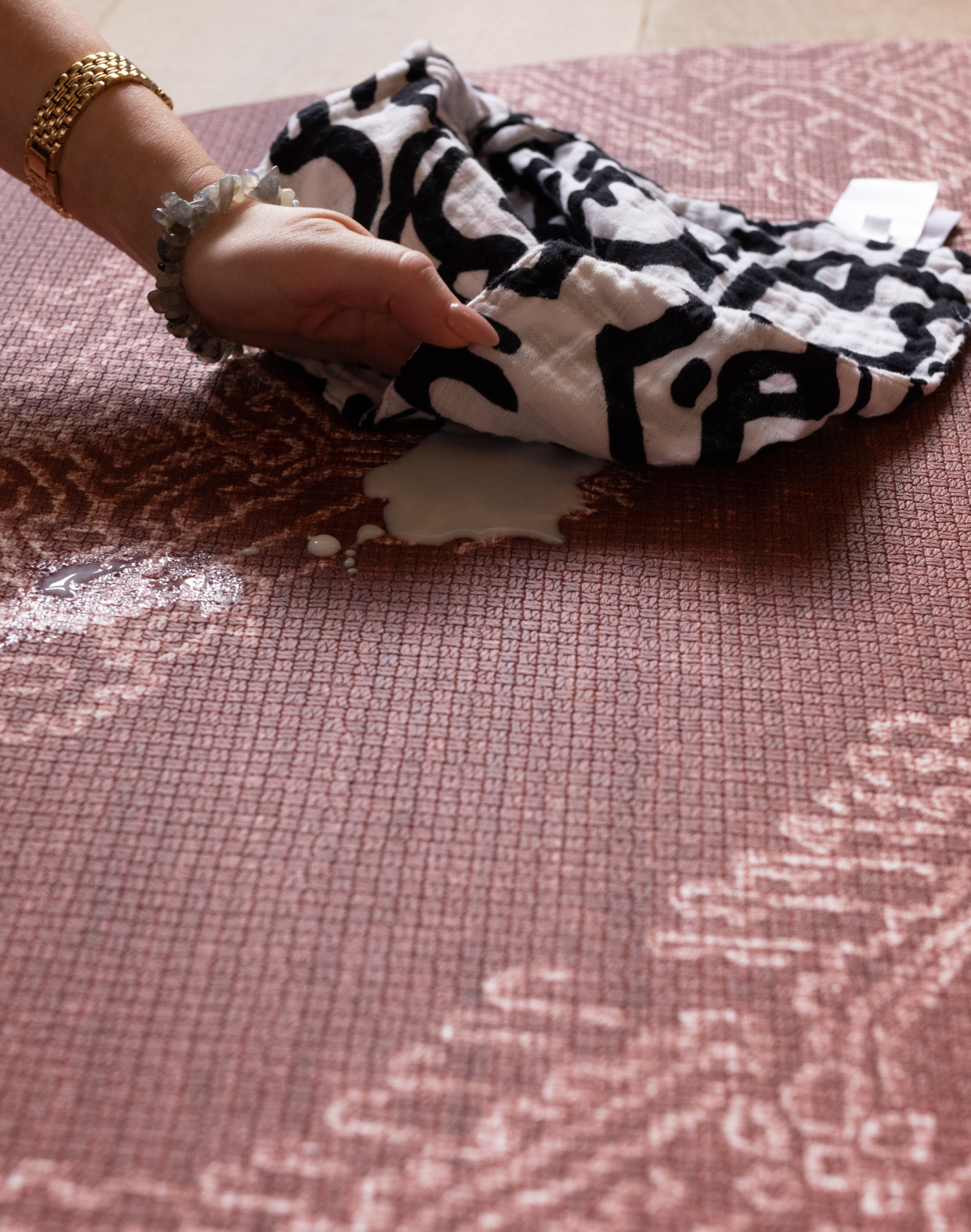 hand wipes up milk spill on surface of red play mat with intricate batik motif to creating a playmat that looks like a rug but practical for family homes