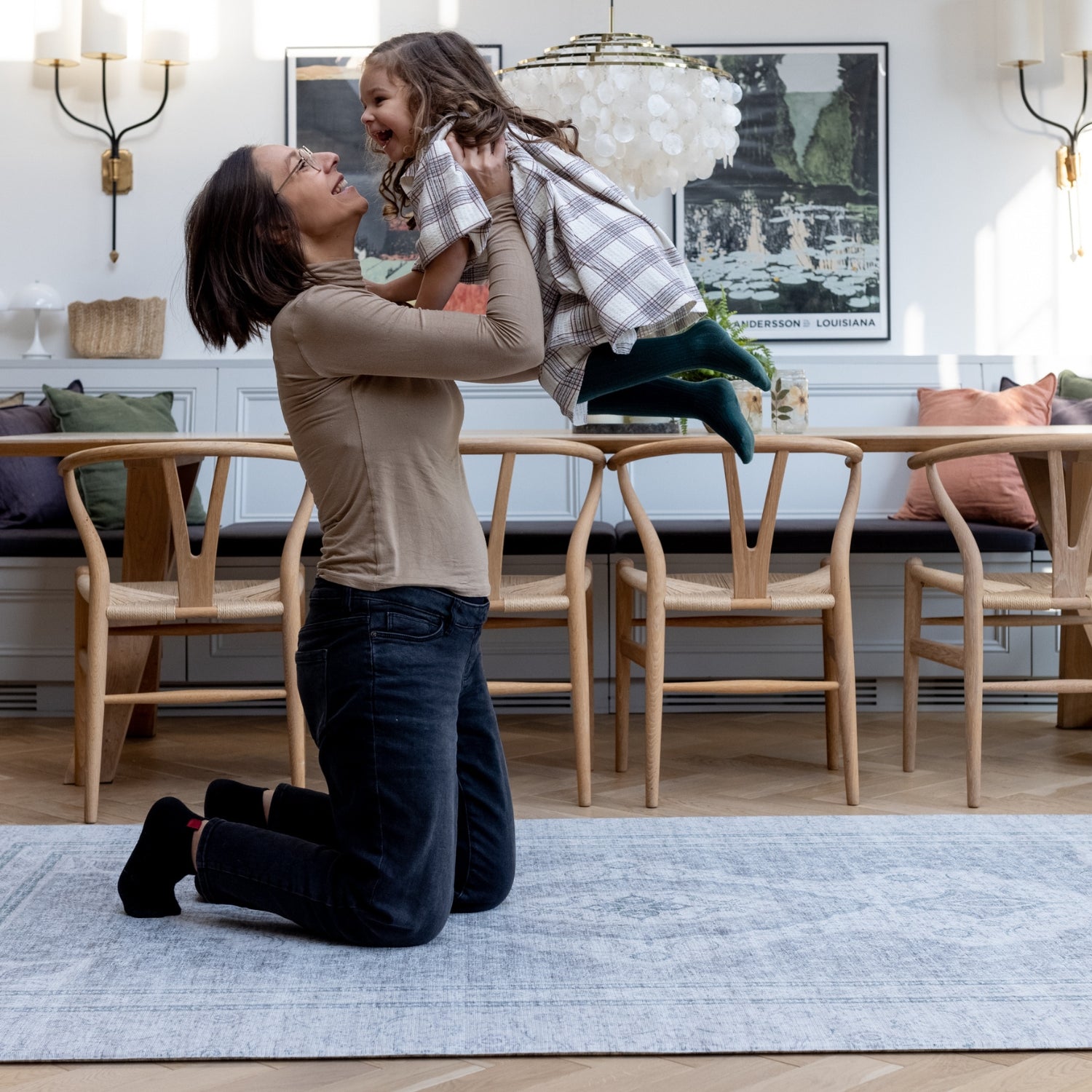 A mom lifts up her child while they play on a large floor mat for the living room. They are both smiling and laughing