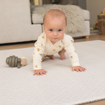 Baby resting on thick floor mat with wooden toy