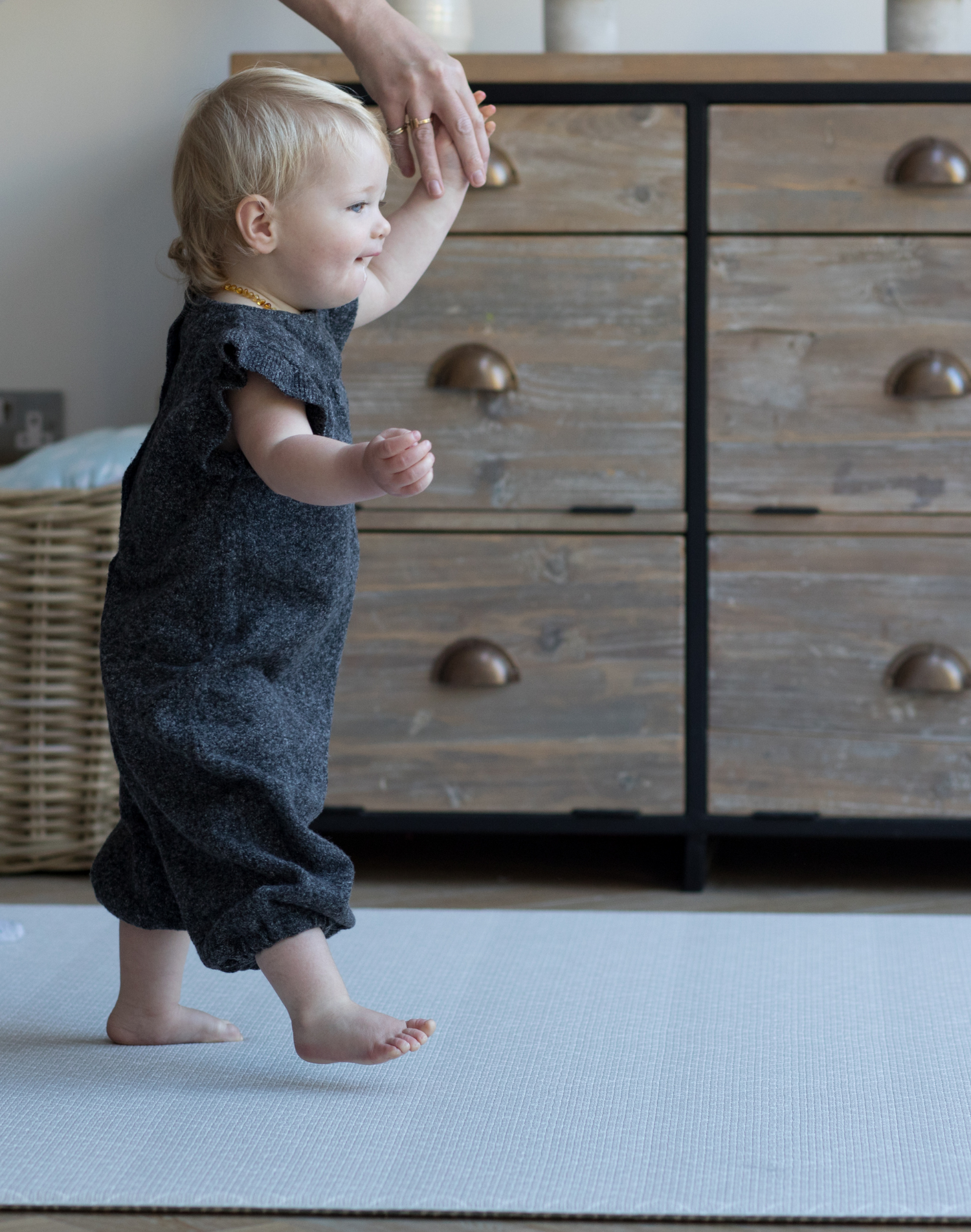 Toddler walks across thick play mat holding hand of adult for extra support