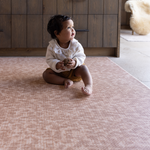 Baby girl sits supported on textural orange play mat with an animal print motif that is subtle and modern thick memory foam offers protection for play time on the floor