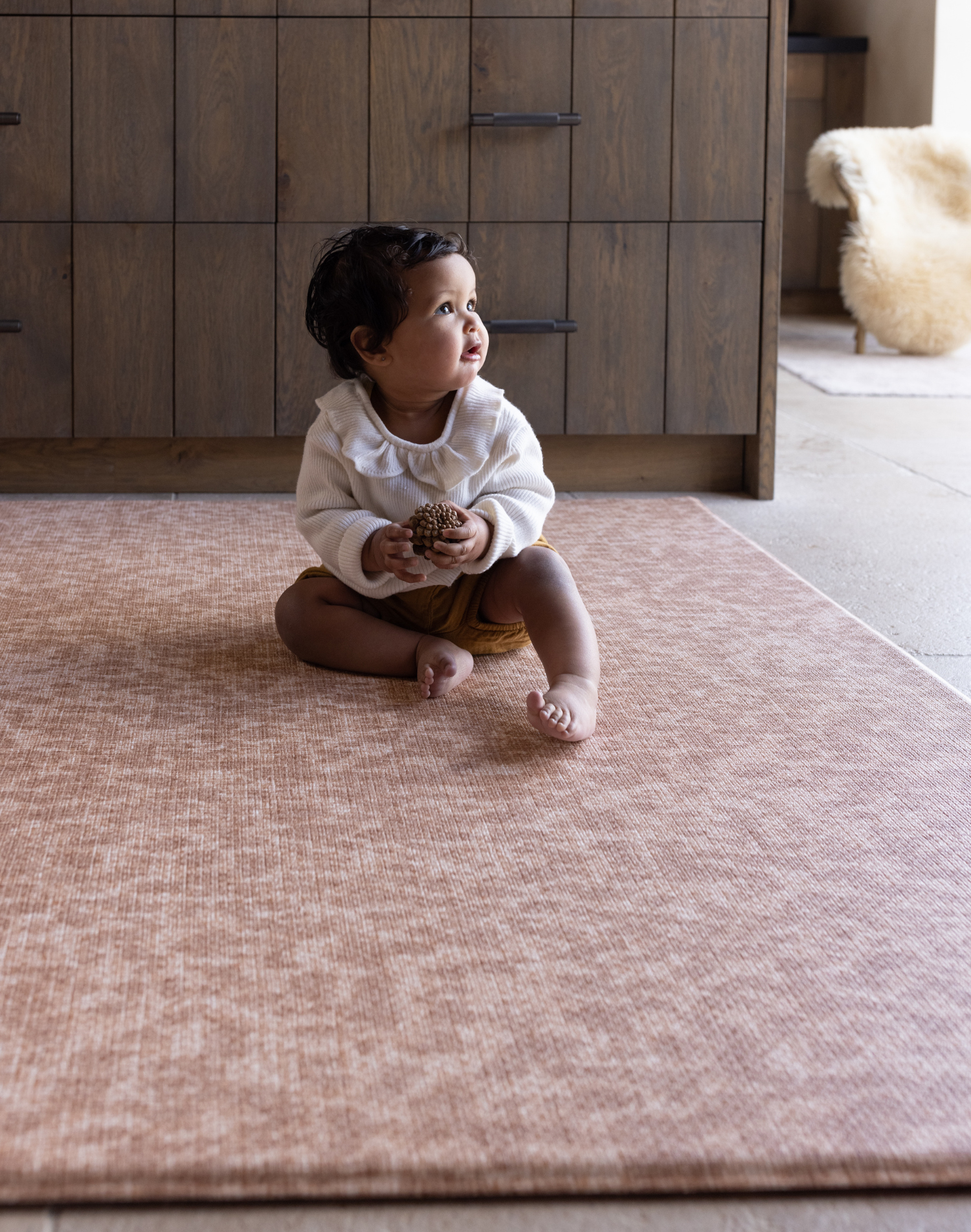 Baby girl sits supported on textural orange play mat with an animal print motif that is subtle and modern thick memory foam offers protection for play time on the floor