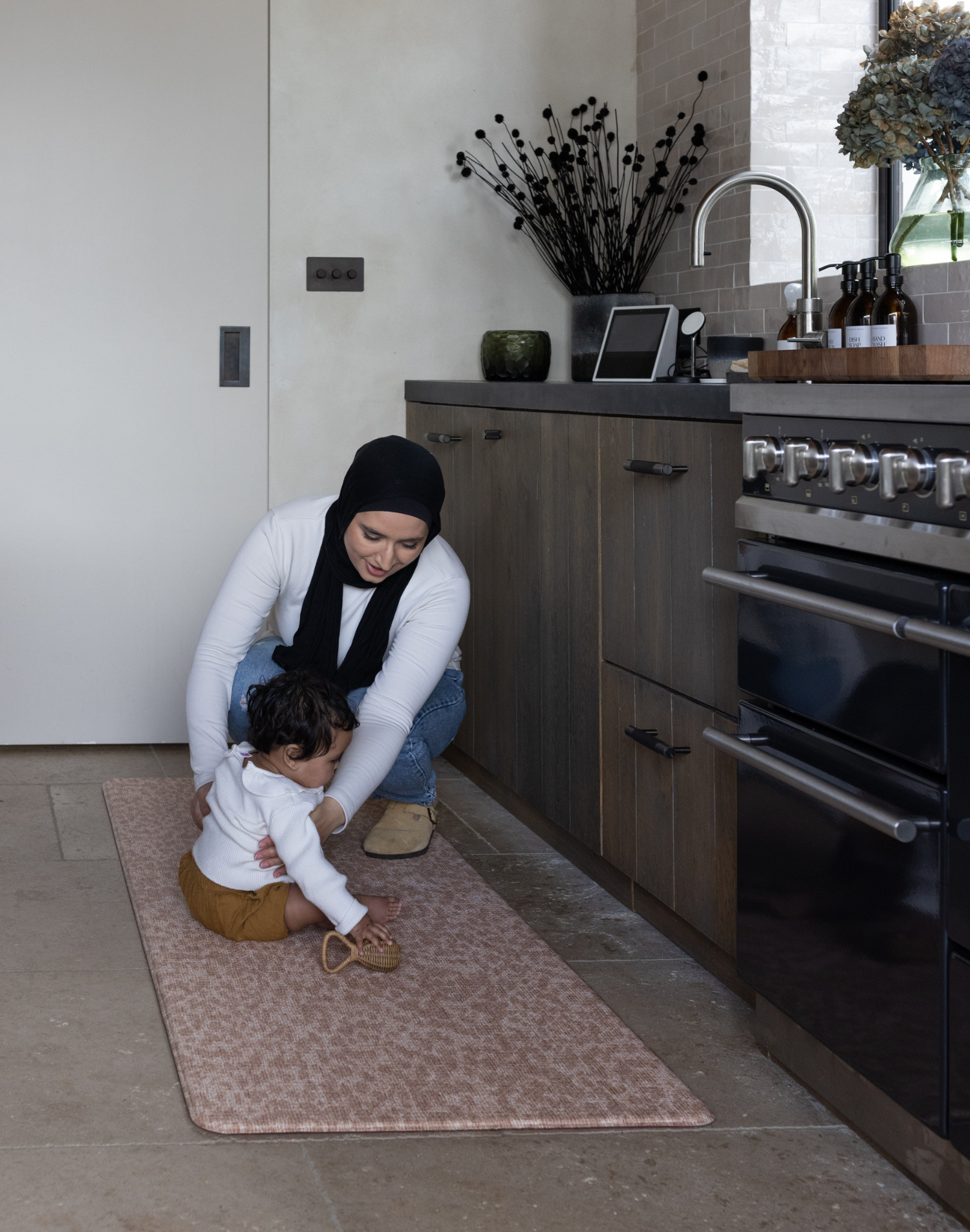 Mom and baby enjoy time together in the kitchen keeping comfortable on the kitchen mat rusa with a gentle leopard print that looks stylish with a thick memory foam design for comfort and protection on kitchen tiled flooring