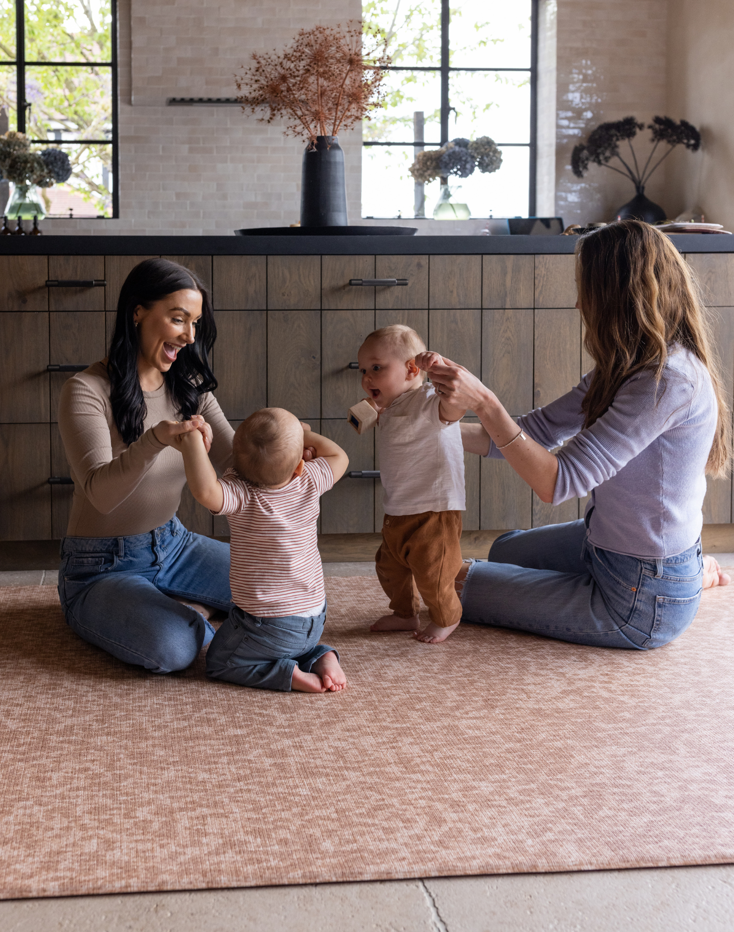 Babies and moms enjoy play time in the kitchen on the protective foam surface of the orange Rusa play mat designed to look beautiful in homes while allowing the family to take to the floor in comfort