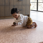 Little girl crawls on extra large play mat holding onto pine cone thick memory foam allows for freedom of movement protecting little joints during milestone developments 