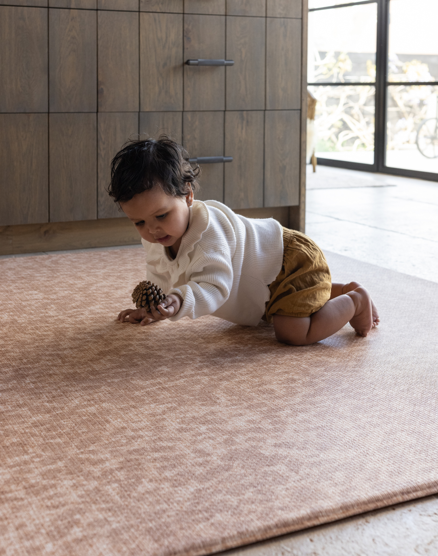 Little girl crawls on extra large play mat holding onto pine cone thick memory foam allows for freedom of movement protecting little joints during milestone developments 