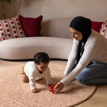 Mom and baby play together on the round Rusa play mat in a subtle orange tone to complement modern spaces with comfortable memory foam to make play time more enjoyable 