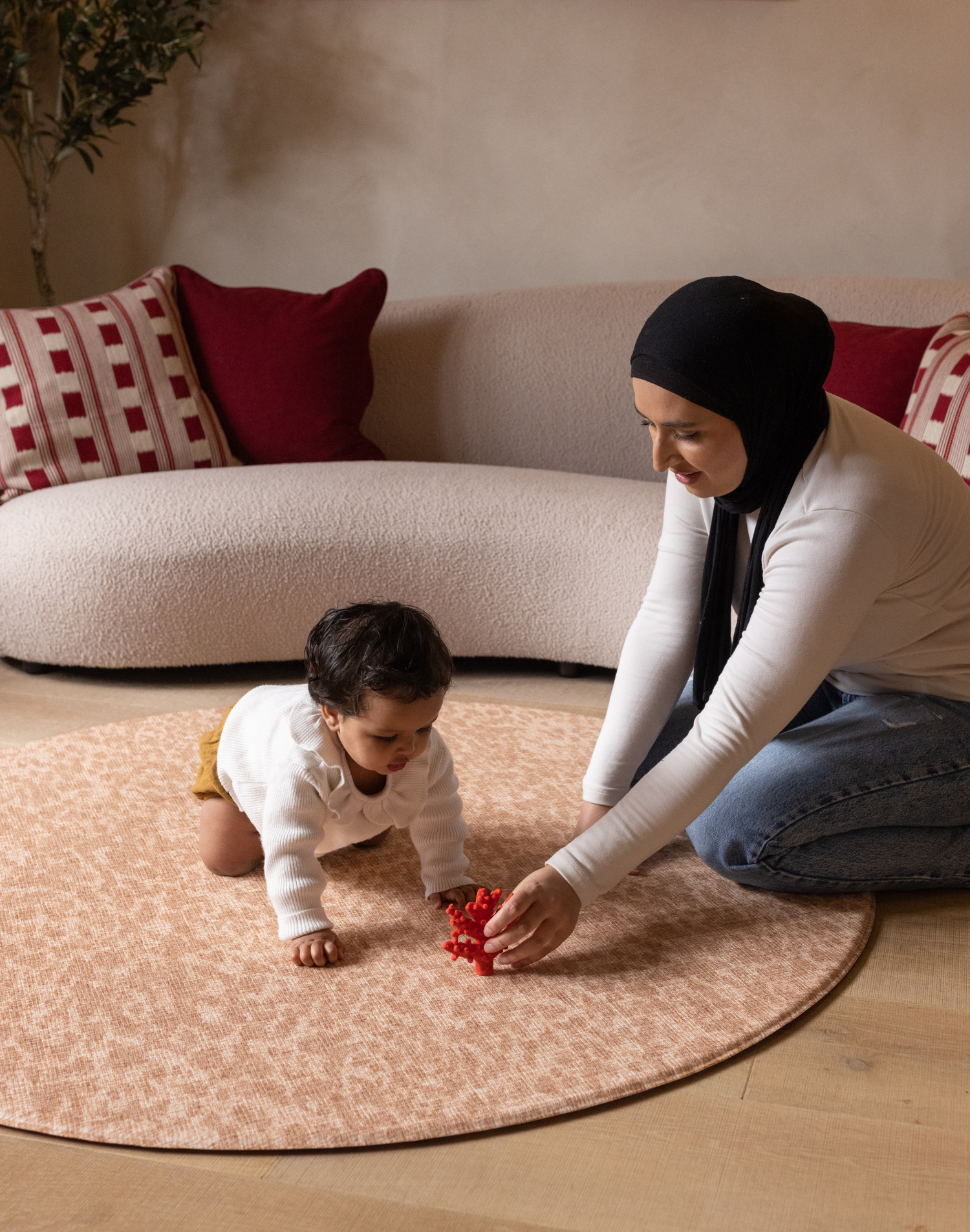 Mom and baby play together on the round Rusa play mat in a subtle orange tone to complement modern spaces with comfortable memory foam to make play time more enjoyable 