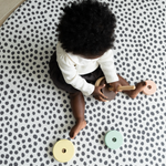 Baby girl enjoys playtime with a wooden stacking toy protected on the floor with the round foam play mat