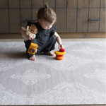 Toddler stacks wooden pebbles on the stable sealed gray sepi play mat with a hand drawn design inspired by heirloom textiles a perfect pick for modern family homes adding practicality and texture