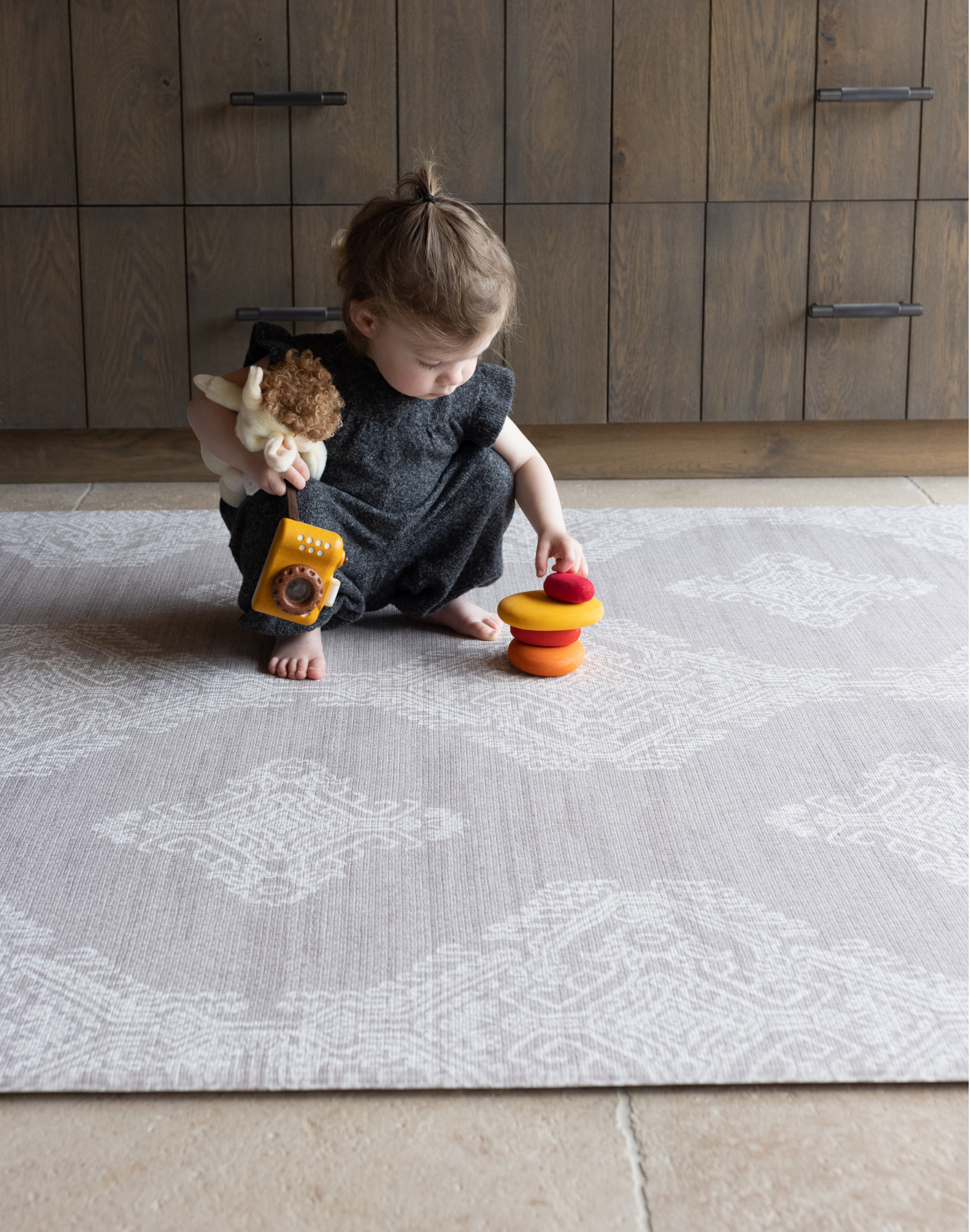 Toddler stacks wooden pebbles on the stable sealed gray sepi play mat with a hand drawn design inspired by heirloom textiles a perfect pick for modern family homes adding practicality and texture