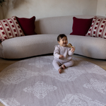 Baby sits on round gray sepi play mat with thick memory foam to support and protect from falls and tumbles