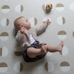 Little baby rolls during floor play with a cushy tan play mat as the ideal play base