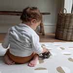 Baby is supported on baby play rug with a neutral organic motif that is beautiful in family homes