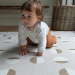 Little baby crawls across a tan play mat with modern motif and non toxic durable design