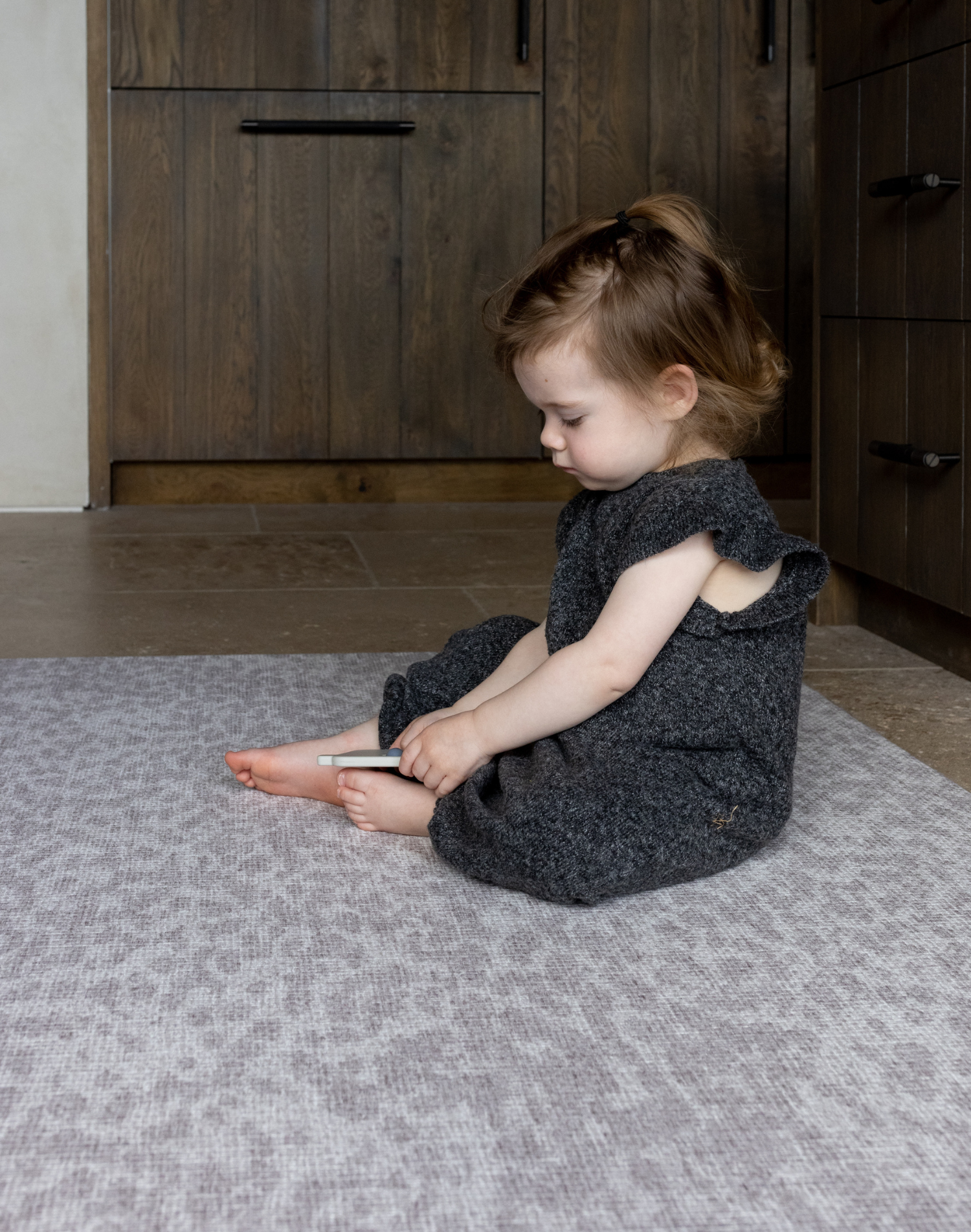 Toddler sits comfortably on cushy gray play mat with a modern neutral play mat design that looks stylish in large family kitchen spaces 