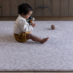 Baby sits unaided on thick supportive gray play mat with textured surface to add supportive and traction during floor time activities 