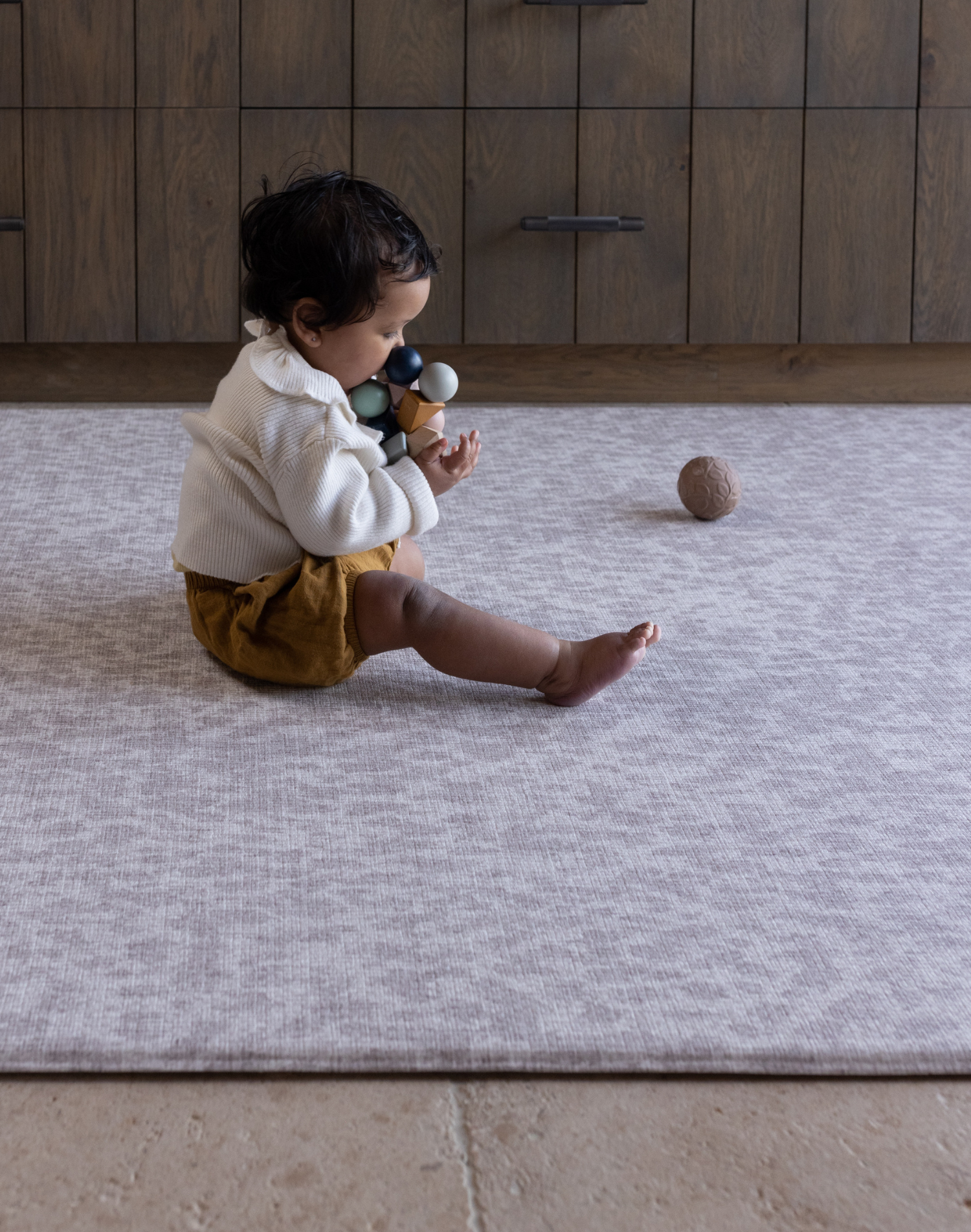 Baby sits unaided on thick supportive gray play mat with textured surface to add supportive and traction during floor time activities 