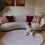 Baby sits on large round gray play mat the sunda a portable play mat size for anywhere in the home with supportive foam design to protect from tumbles and falls