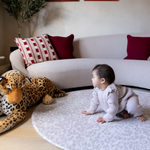 Baby crawls on padded crawling mat with subtle gray leopard print design and large soft toy in stylish modern family home