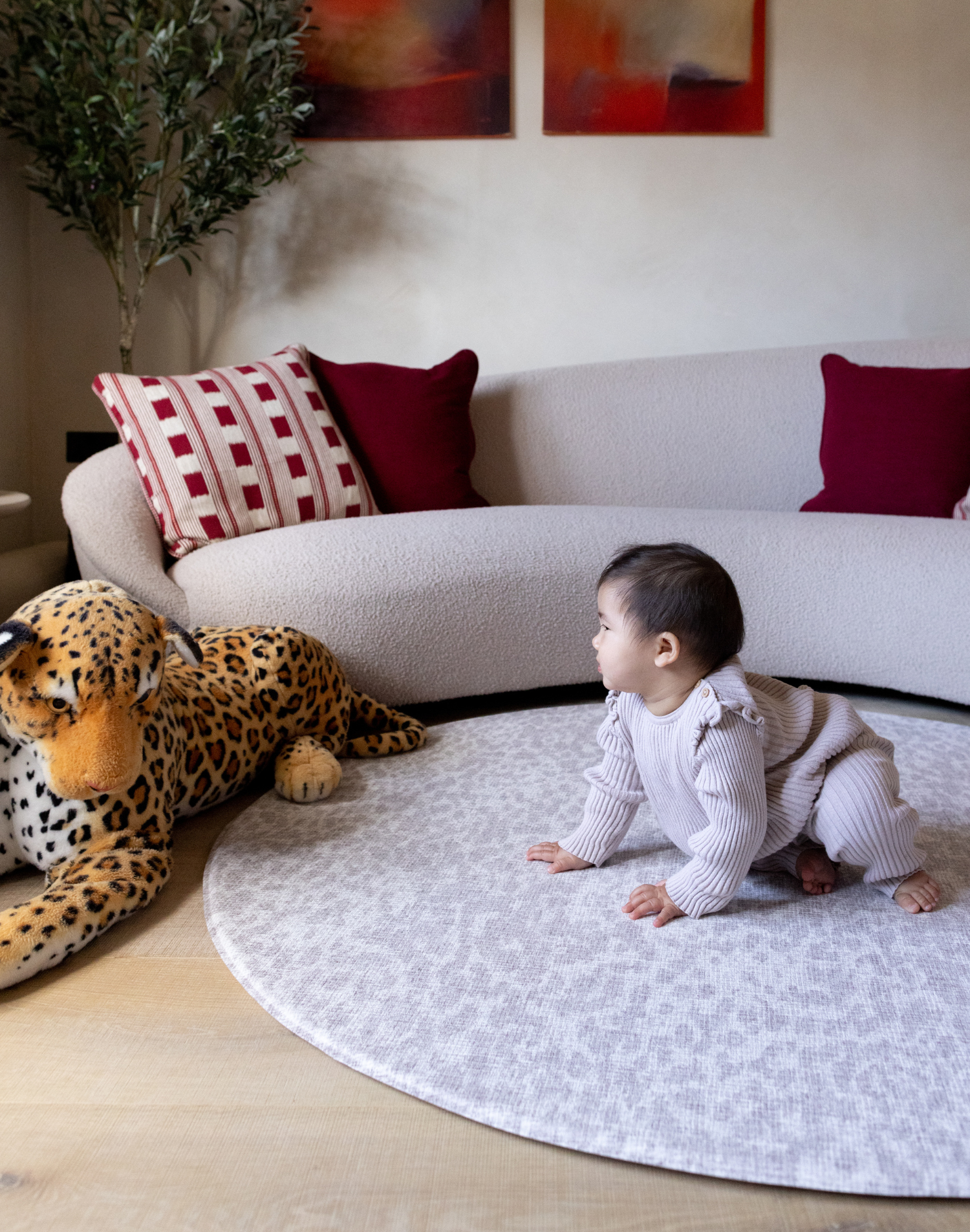 Baby crawls on padded crawling mat with subtle gray leopard print design and large soft toy in stylish modern family home