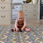 Baby sitting on iconic Strawberry Thief design play mat with thick memory foam to support and protect on hard wood flooring playing with pine cones