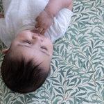 Baby laying relaxed on Willow Boughs play mat by Totter and Tumble in collaboration with heritage design group Morris & Co. keeping babies comfy for floor play and supporting developmental milestones